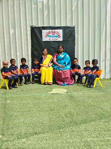 Teachers seated with students, school signage visible